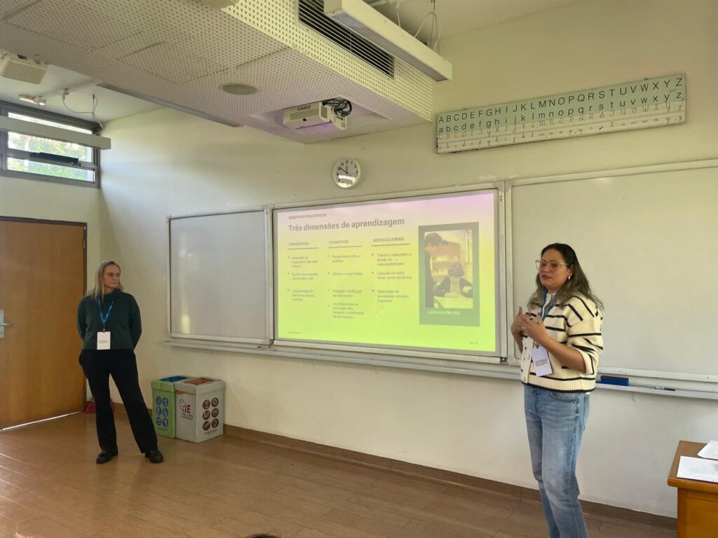 Apresentação do projeto de jornal escolar bilíngue pelas professoras, exibindo em sala de aula os slides sobre as três dimensões de aprendizagem.